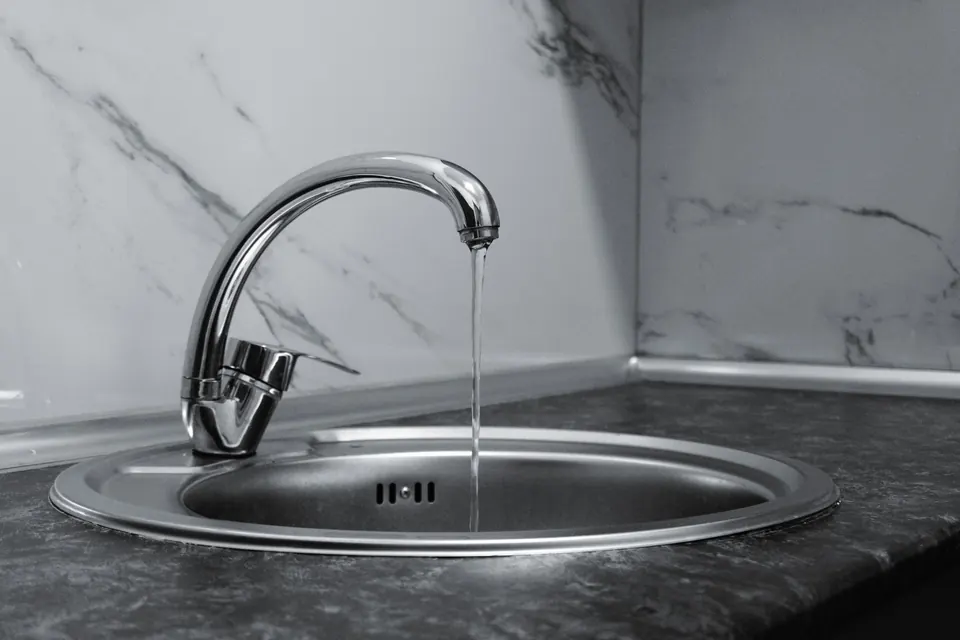 A chrome kitchen faucet running water into a stainless steel sink