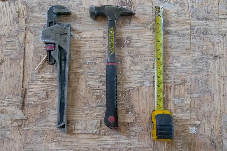 A pipe wrench, hammer and tape measure hanging on a workshop wall