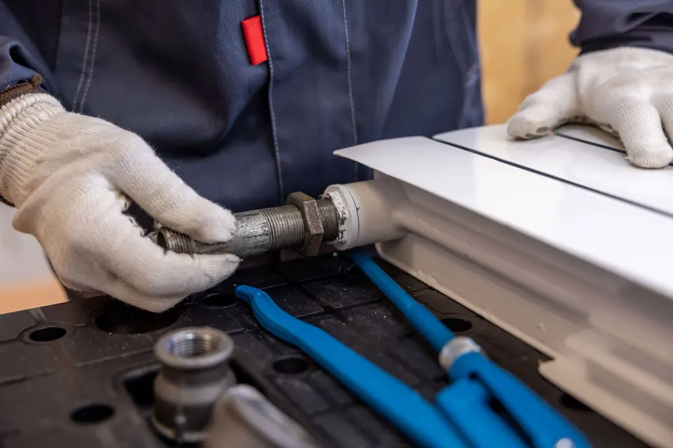 A plumber in work gloves fitting a pipe connection with hand tools
